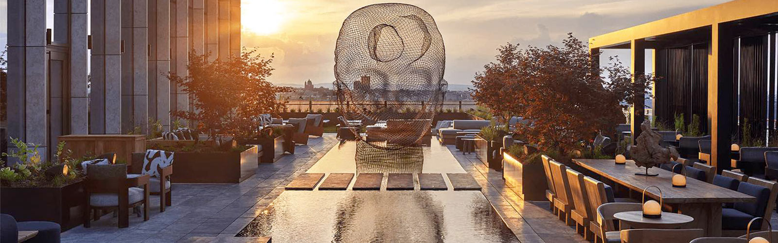 Dazzling view of the sunset from the balcony of the Equinox Hotel with multiple cozy seating areas and a modern wire sculpture over a water feature.