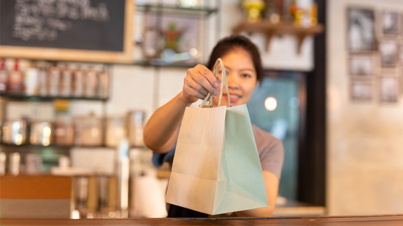 Smiling woman handing to-go bag over the counter.